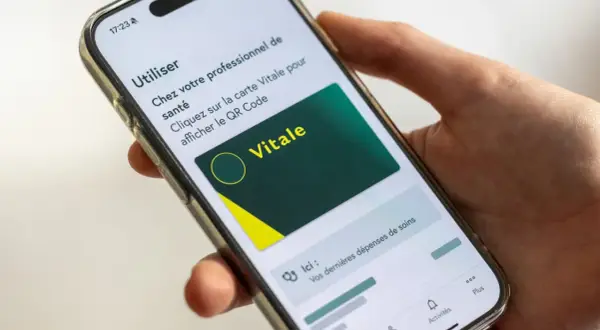 Main d'une personne tenant un smartphone affichant la carte Vitale numérique. Idéal pour le courrier restitution carte vitale.