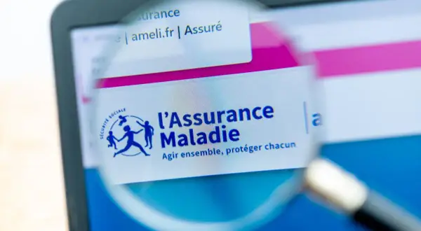 Loupe sur l'écran d'un ordinateur affichant le site ameli.fr, logo de l'Assurance Maladie. Une lettre demande d'ouverture des droits à l'assurance maladie est en cours de consultation.