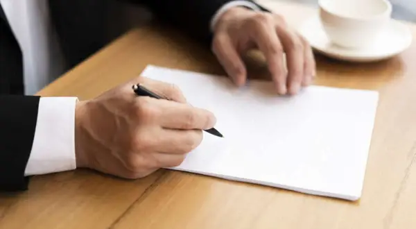 Homme en costume écrivant une lettre. Il pourrait s'agir d'une démarche concernant le harcèlement moral, avec l'aide de la médecine du travail.