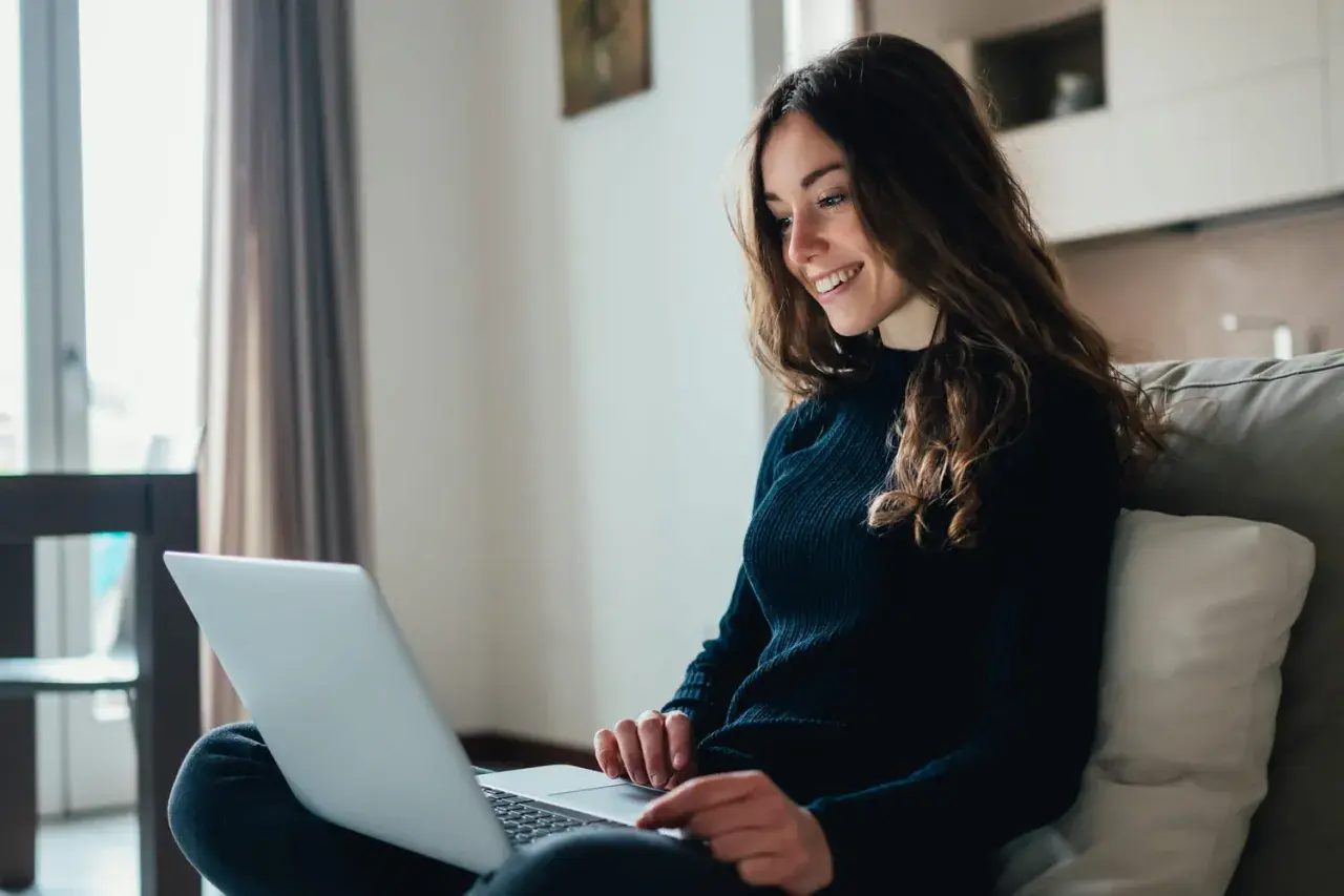 Jeune femme souriante travaillant sur son ordinateur portable, rédigeant sa lettre de motivation master MEEF.