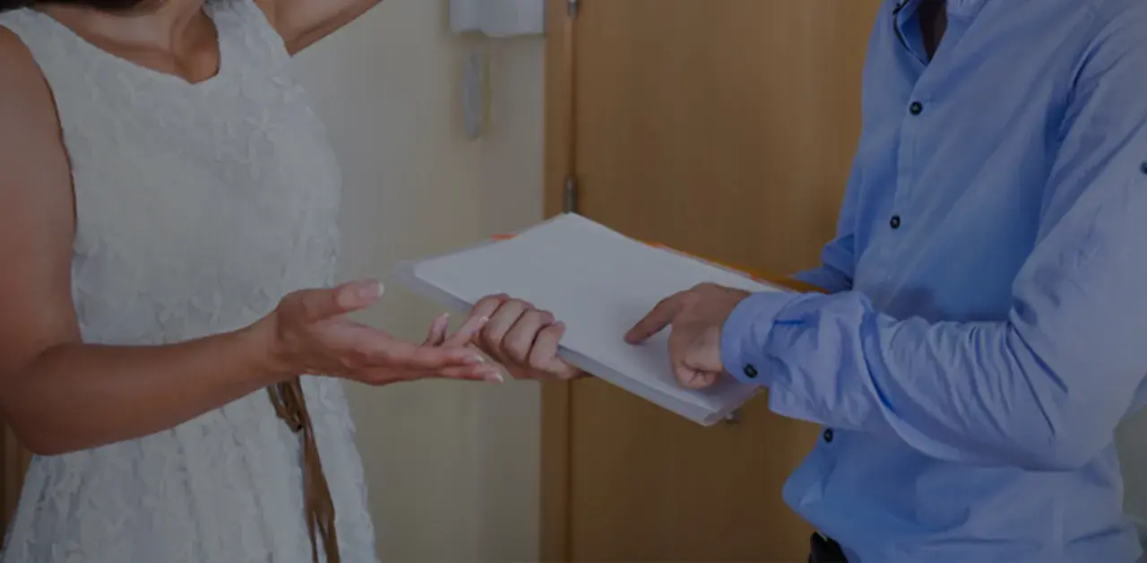 Une femme en robe blanche reçoit des documents d'un homme en chemise bleue.