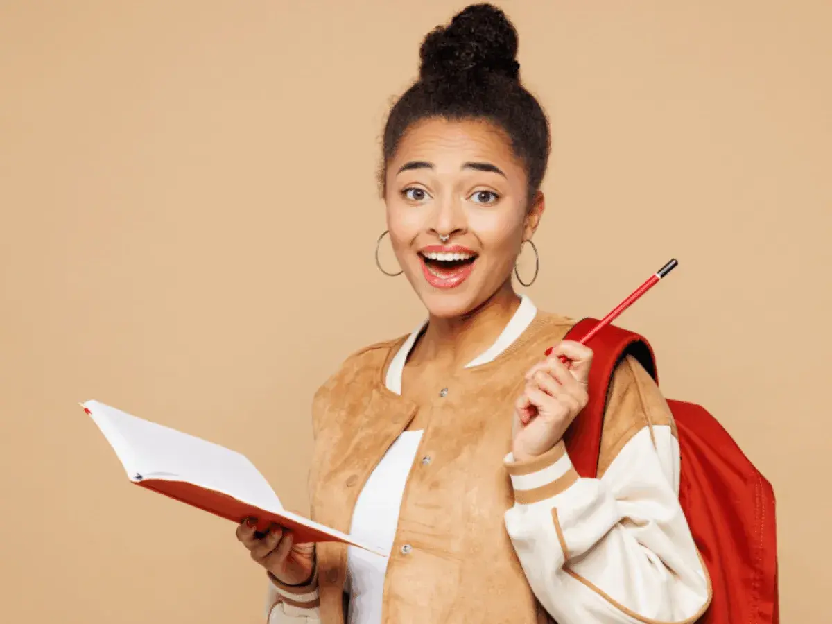 Jeune femme souriante avec un livre et un crayon, prête pour sa lettre de motivation stage à l'étranger.
