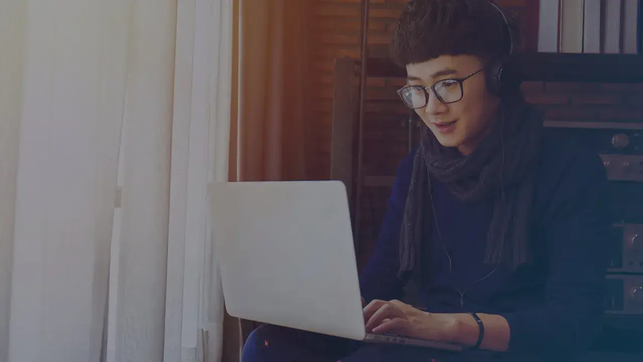 Jeune homme avec des écouteurs et des lunettes travaille sur son ordinateur portable, rédigeant une lettre de motivation intérim sans expérience.