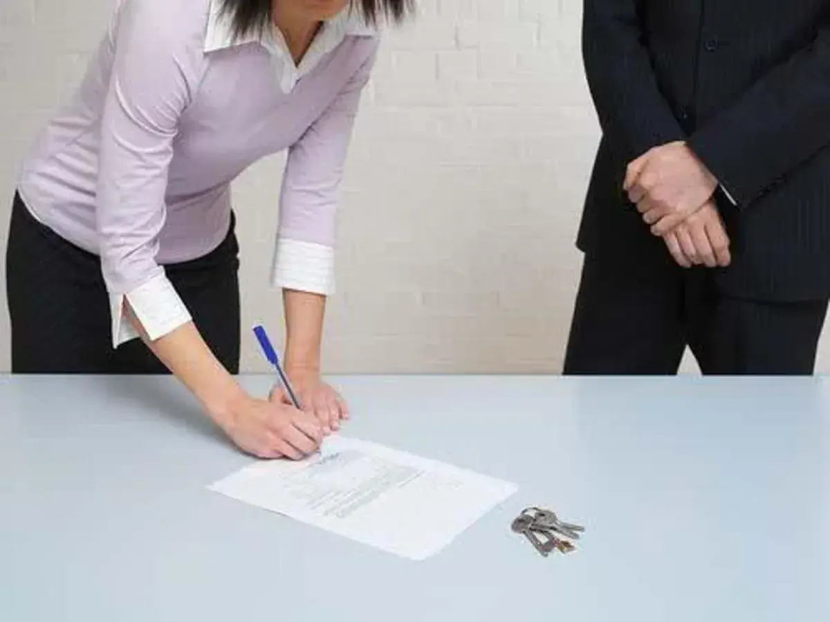 Une femme signe un document, peut-être un modèle lettre demande pour préjudice subi. Des clés sont posées sur la table.