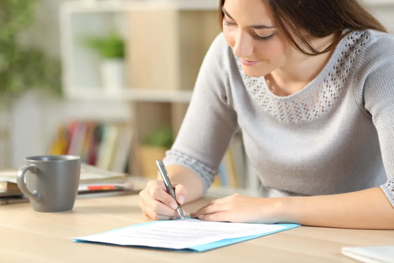 Femme écrivant une lettre de motivation sur un bureau avec une tasse de café.