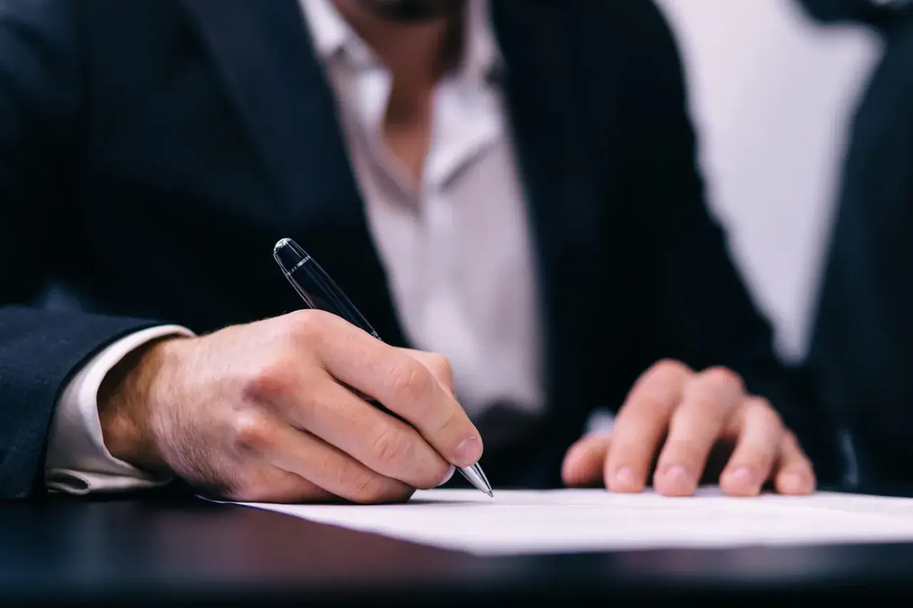 Un homme en costume signe un document, peut-être un modèle lettre demande d'exonération.