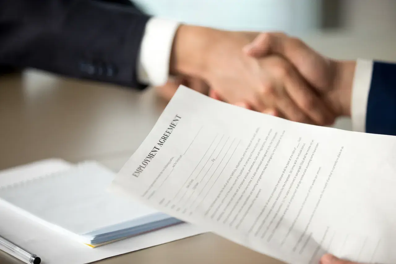 Poignée de main après la signature d'un contrat. Une lettre de motivation pour un poste d'assistant manager est visible.