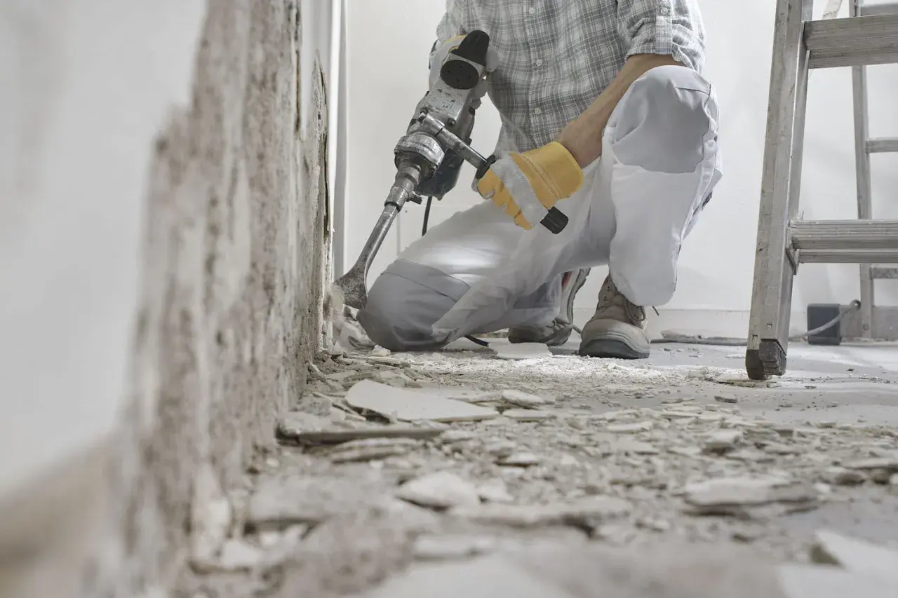 Un ouvrier utilise un marteau-piqueur pour démolir un mur. Des débris jonchent le sol. C'est une étape de travaux, comme dans une lettre d'information.