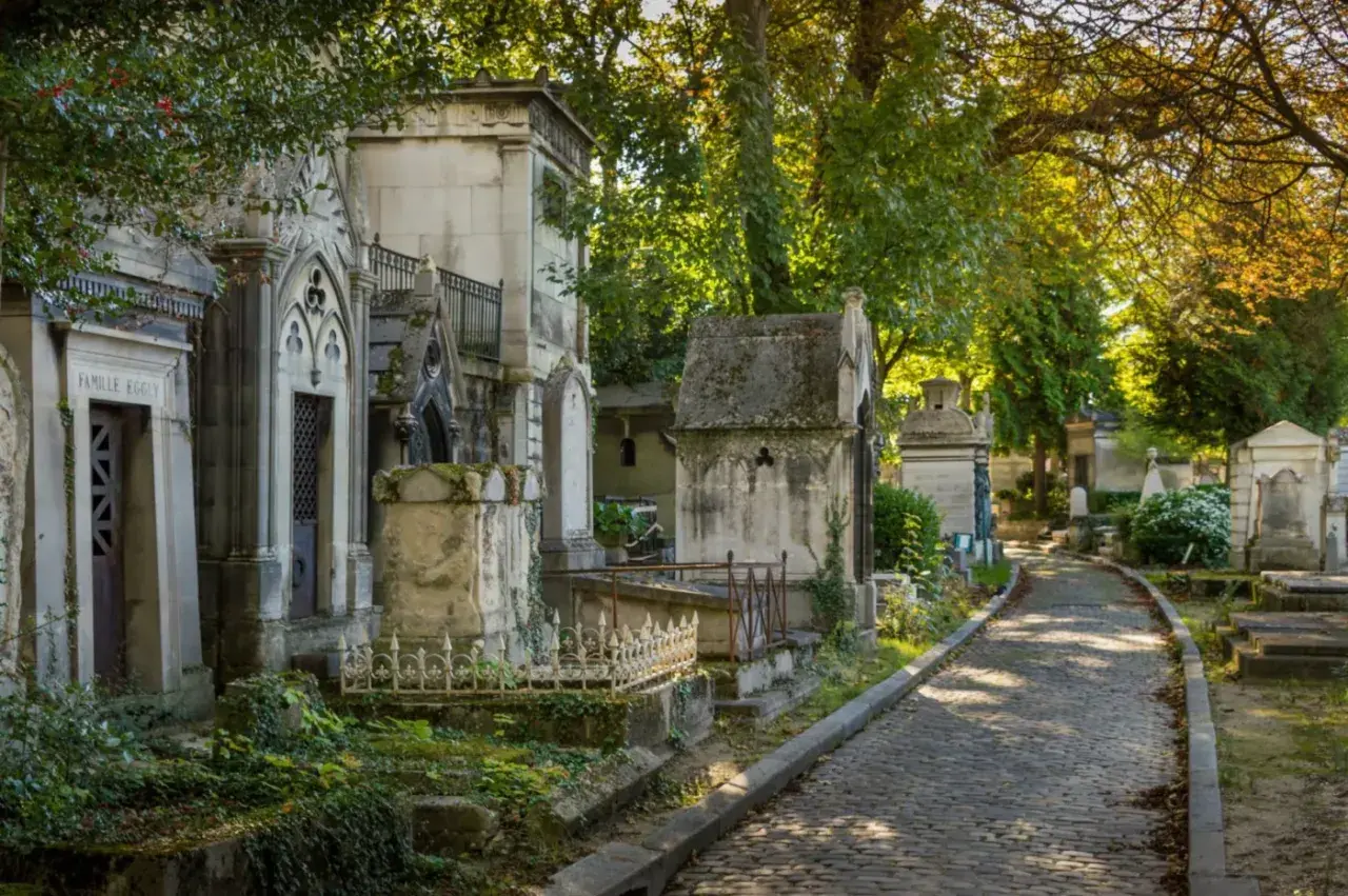 Allée pavée dans un cimetière verdoyant, bordée de mausolées. Idéal pour un modèle de lettre pour renouvellement de concession cimetière.