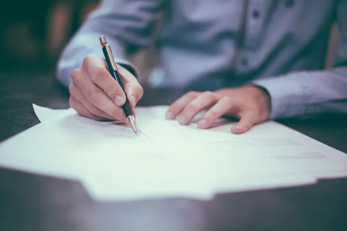 Main tenant une plume, écrit sur un document.