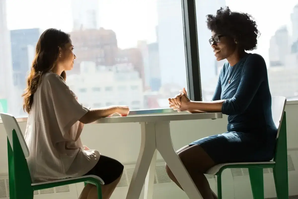 Deux femmes discutent à une table, l'une semble faire une demande d'entretien avec son directeur.