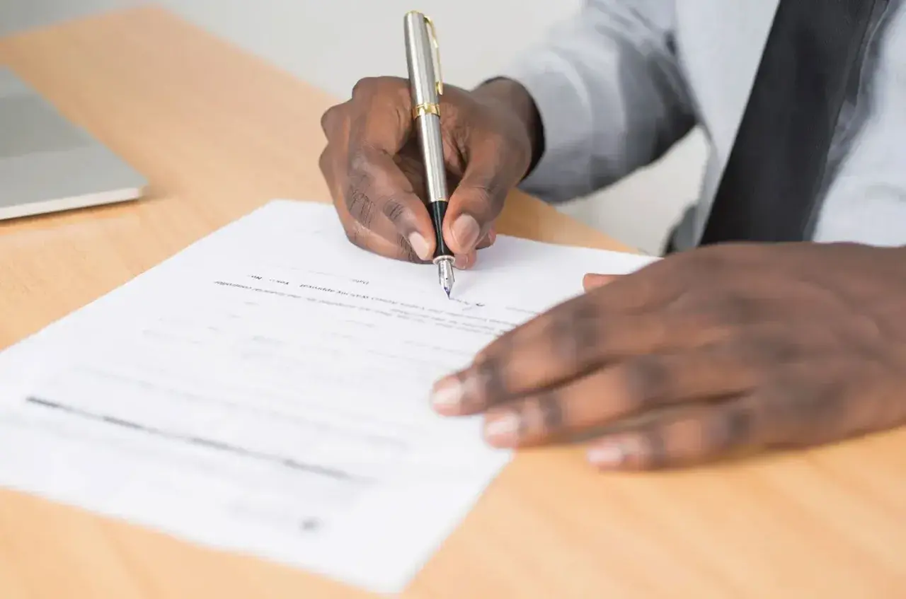 Main noire signant un document, peut-être une lettre de motivation pour un poste d'électrotechnicien.