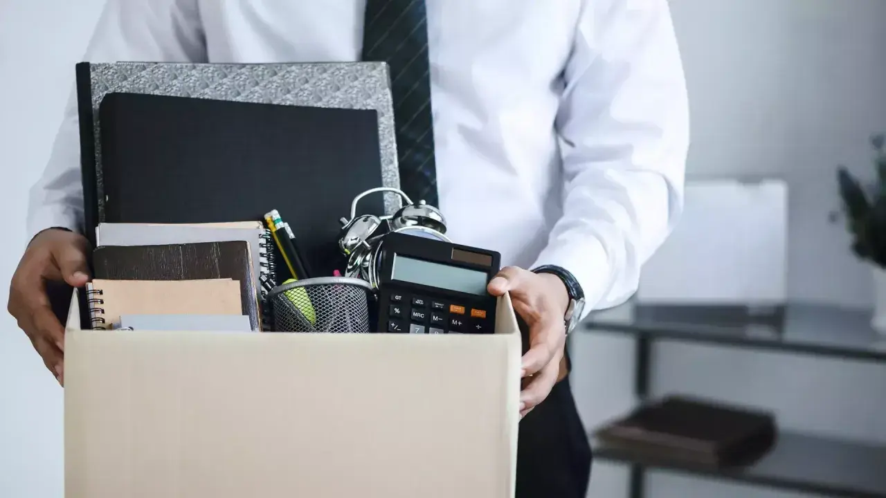 Un étudiant quitte son emploi, portant une boîte remplie d'objets de bureau, symbolisant une lettre de démission contrat étudiant sans préavis.