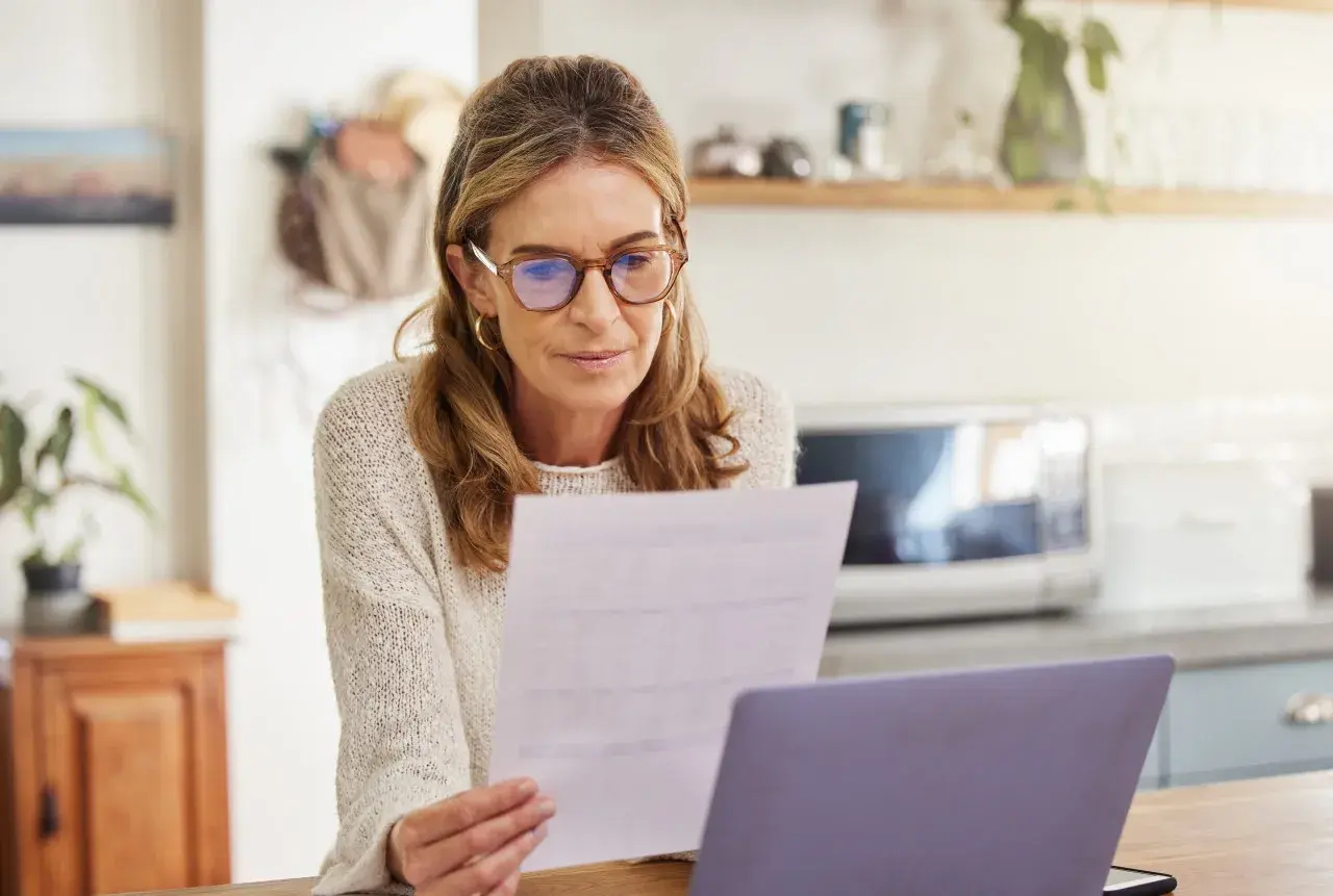 Femme concentrée sur un document, peut-être un modèle lettre déclaration tardive impôts, devant son ordinateur.