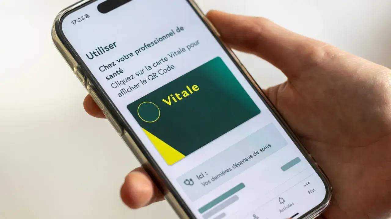 Main d'une personne tenant un smartphone affichant la carte Vitale numérique. Idéal pour le courrier restitution carte vitale.
