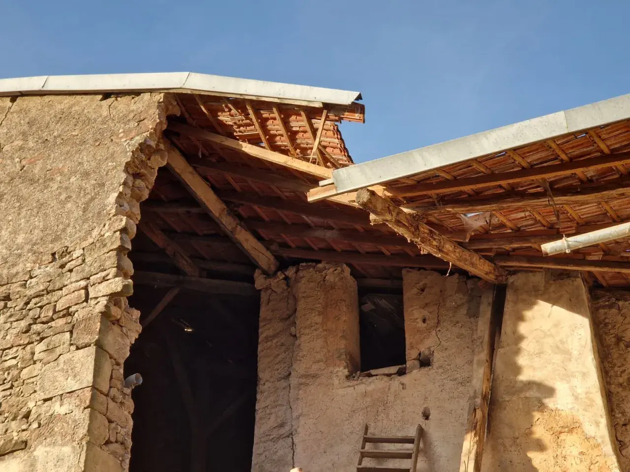 Mise en demeure : mur écroulé du voisin. Bâtiment en ruine, toiture endommagée, ciel bleu.