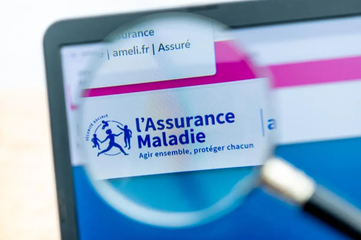 Loupe sur l'écran d'un ordinateur affichant le site ameli.fr, logo de l'Assurance Maladie. Une lettre demande d'ouverture des droits à l'assurance maladie est en cours de consultation.
