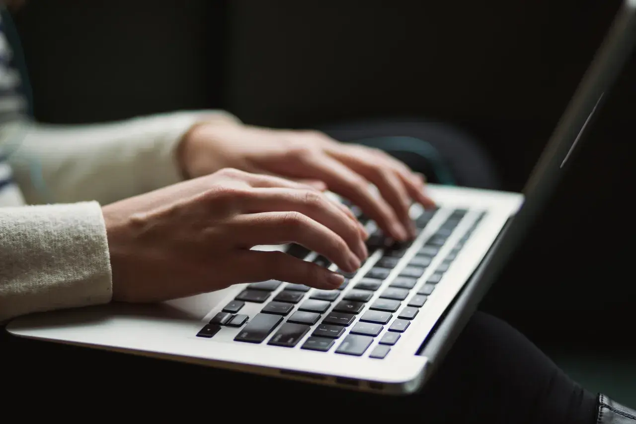 Mains tapotant sur un clavier d'ordinateur portable, rédigeant une lettre au maire pour une demande d'aide.