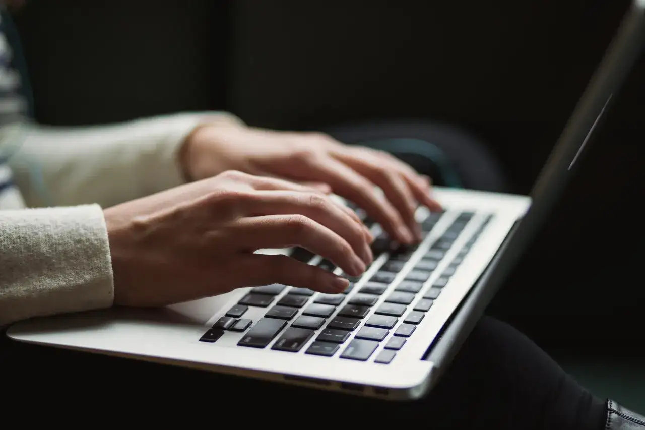 Mains tapotant sur un clavier d'ordinateur portable, rédigeant une lettre au maire pour une demande d'aide.
