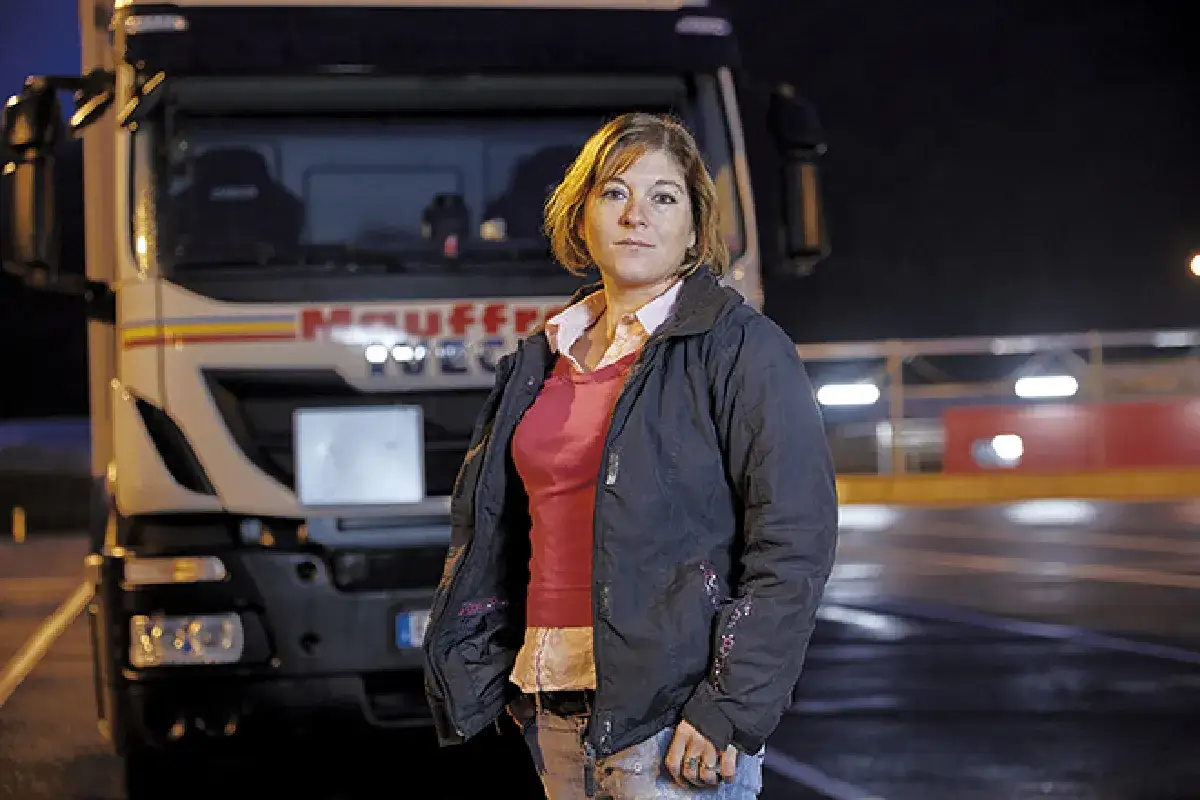 Femme chauffeur poids lourd, prête à rédiger sa lettre de motivation. Camion Iveco en arrière-plan.