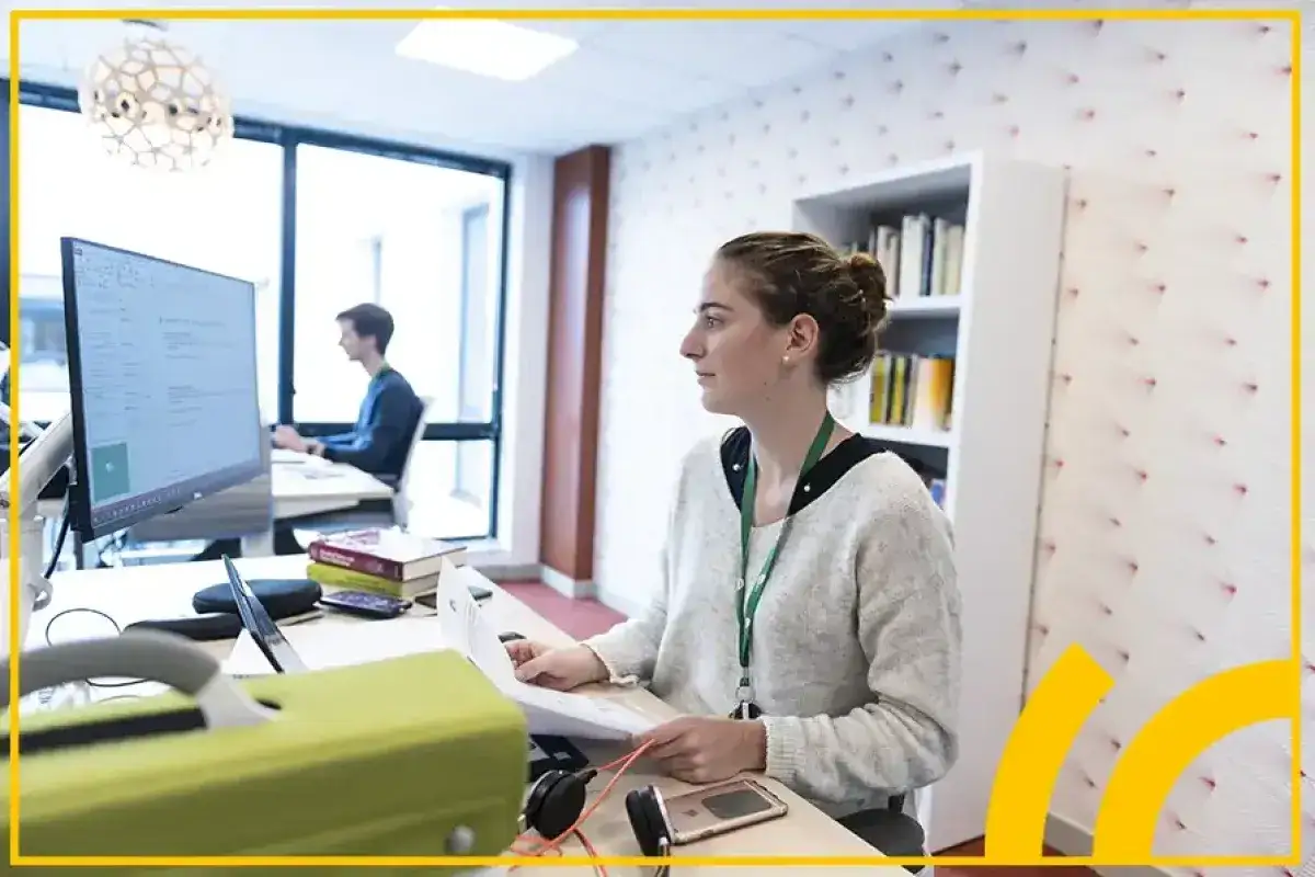 Jeune femme travaillant sur sa lettre de motivation alternance, entourée de documents et d'un ordinateur.