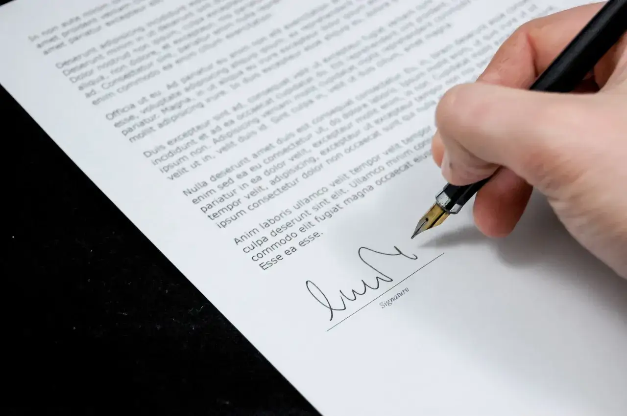 Signature sur un document, peut-être un désistement appartement. Une main tient un stylo plume pour signer.