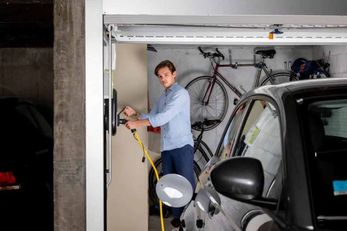 Un homme branche sa voiture électrique dans un garage. Il pense à son droit à la prise copropriété, lettre type en tête.