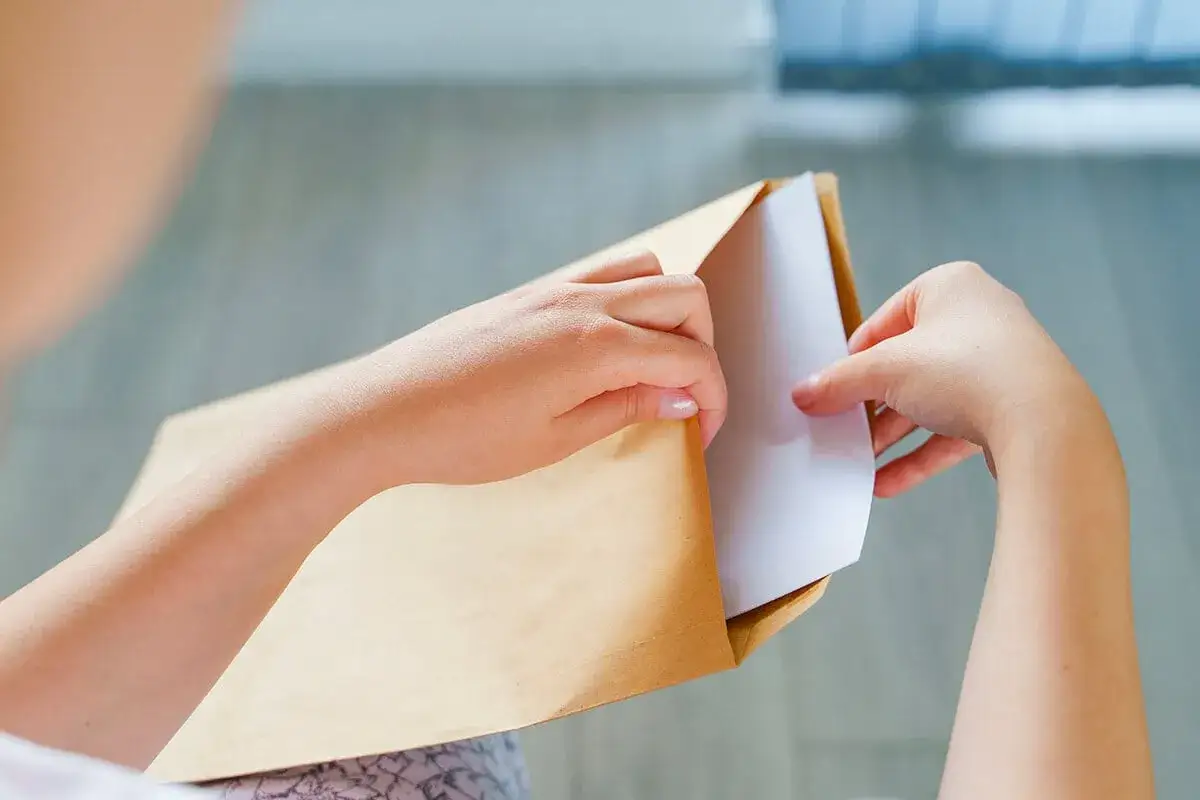 Mains ouvrant une enveloppe marron. Peut-être pour y trouver un modèle lettre bailleur sociaux pour travaux.