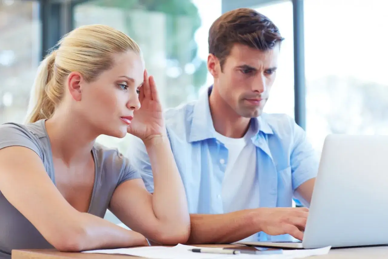 Couple concentré sur un ordinateur, peut-être pour une reclamation caisse epargne. La femme semble soucieuse.