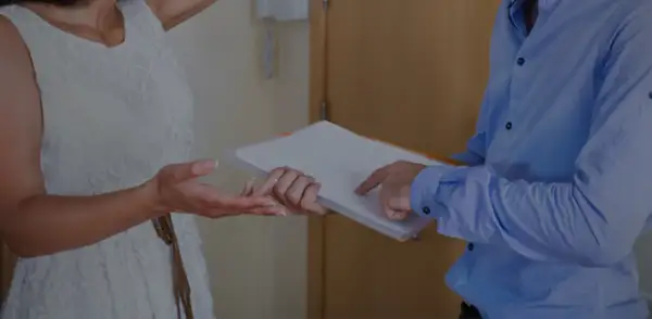 Une femme en robe blanche reçoit des documents d'un homme en chemise bleue.