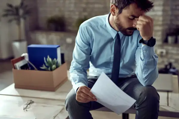 Homme stressé tenant une lettre de plainte au syndic de copropriété, avec une boîte de déménagement derrière lui.