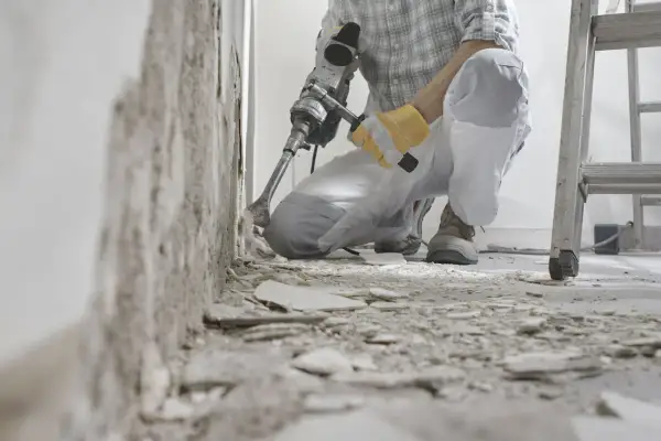 Un ouvrier utilise un marteau-piqueur pour démolir un mur. Des débris jonchent le sol. C'est une étape de travaux, comme dans une lettre d'information.