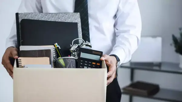 Un étudiant quitte son emploi, portant une boîte remplie d'objets de bureau, symbolisant une lettre de démission contrat étudiant sans préavis.
