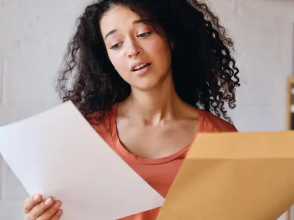Jeune femme perplexe devant sa lettre de motivation Parcoursup. Elle tient un document blanc et une enveloppe marron.