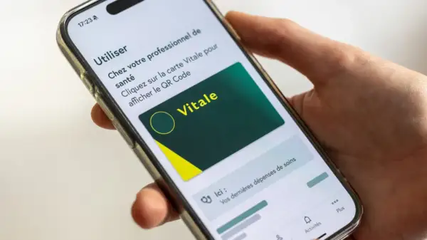 Main d'une personne tenant un smartphone affichant la carte Vitale numérique. Idéal pour le courrier restitution carte vitale.