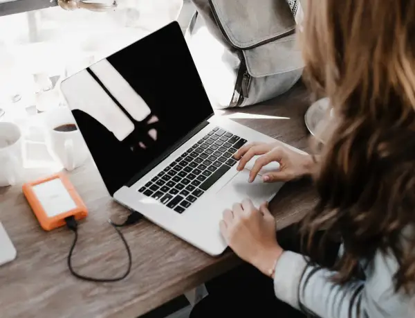 Une personne rédige une lettre de motivation française sur son ordinateur portable, avec une tasse de café et un disque dur externe à proximité.