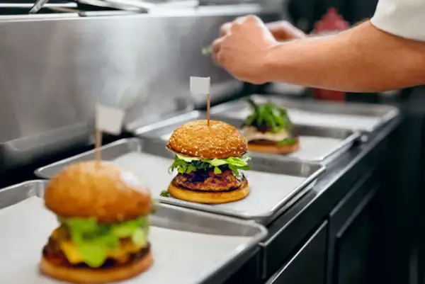 Trois hamburgers appétissants sur des plateaux, prêts pour la livraison. Une image parfaite pour une lettre de motivation restauration rapide.